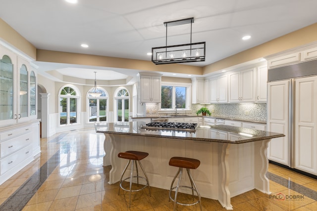 kitchen featuring stainless steel gas stovetop, white cabinetry, a kitchen island, and dark stone counters