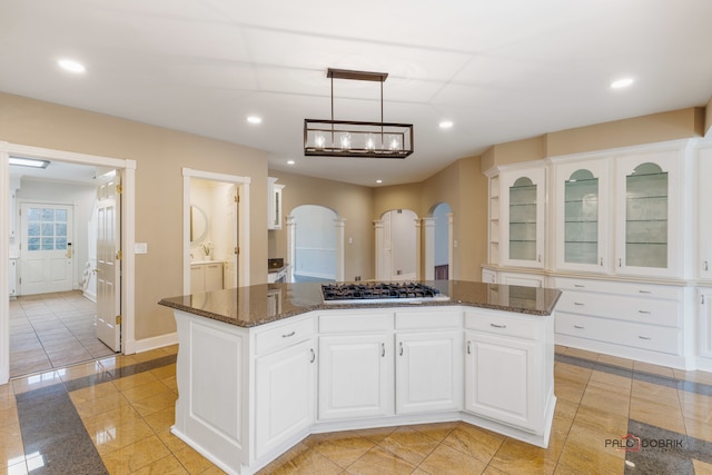 kitchen featuring dark stone countertops, hanging light fixtures, white cabinets, a kitchen island, and stainless steel gas stovetop