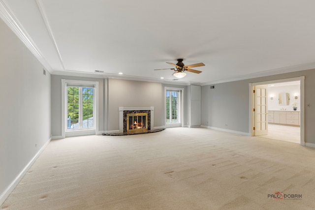 unfurnished living room with a premium fireplace, crown molding, light colored carpet, and ceiling fan