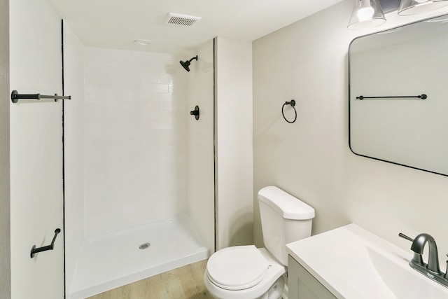 bathroom featuring vanity, toilet, wood-type flooring, and tiled shower