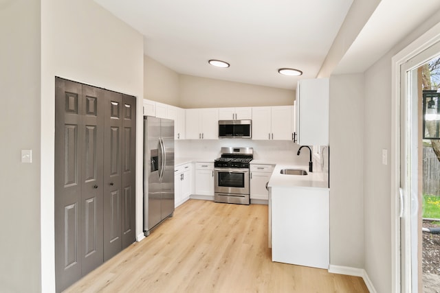 kitchen with appliances with stainless steel finishes, sink, white cabinetry, light hardwood / wood-style floors, and lofted ceiling