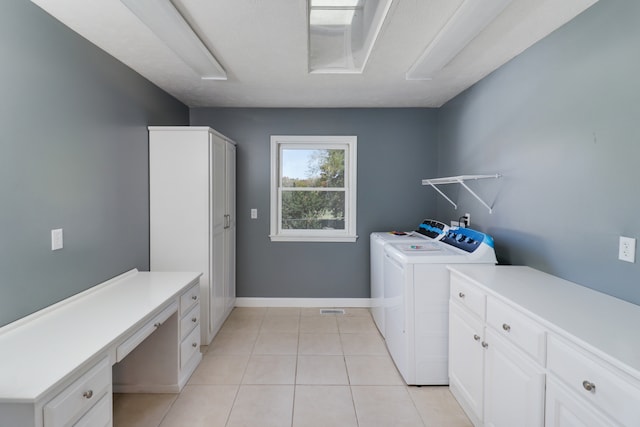 laundry area featuring washer and clothes dryer, light tile patterned floors, and cabinets