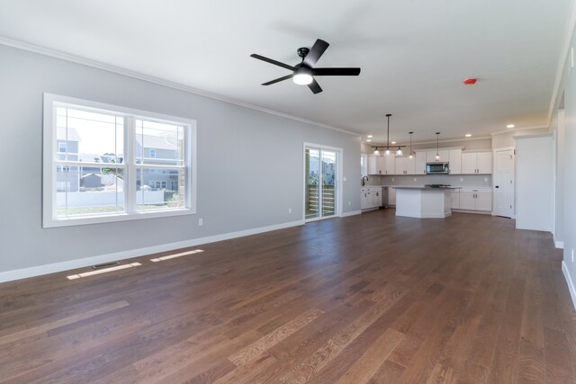 unfurnished living room featuring ceiling fan, a healthy amount of sunlight, dark hardwood / wood-style flooring, and crown molding