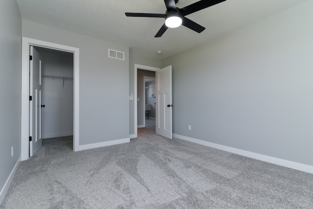 unfurnished bedroom with ceiling fan, a spacious closet, light carpet, and a closet