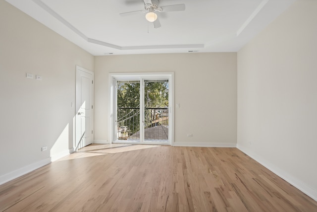 empty room featuring a raised ceiling, light wood-type flooring, and ceiling fan