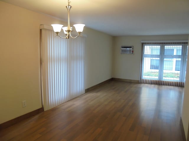 spare room featuring an AC wall unit, a notable chandelier, and dark hardwood / wood-style flooring