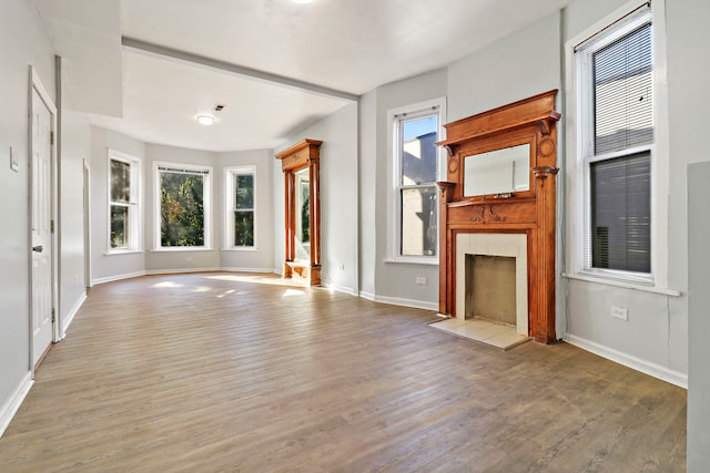 unfurnished living room featuring light wood-type flooring, a tiled fireplace, and a healthy amount of sunlight