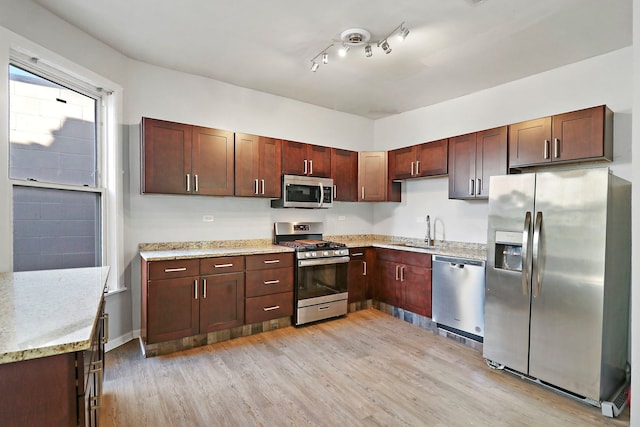 kitchen featuring appliances with stainless steel finishes, sink, light stone counters, and light hardwood / wood-style flooring