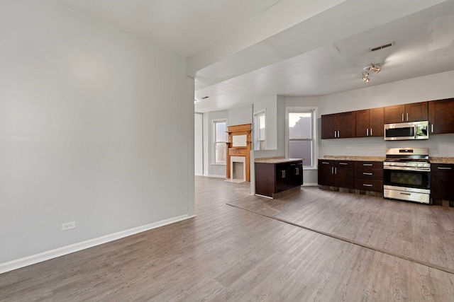 kitchen with dark brown cabinetry, stainless steel appliances, wood-type flooring, and a kitchen island