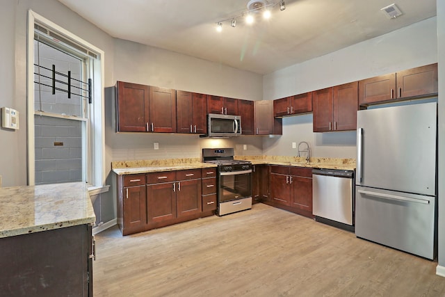 kitchen featuring appliances with stainless steel finishes, light stone counters, light hardwood / wood-style floors, and sink