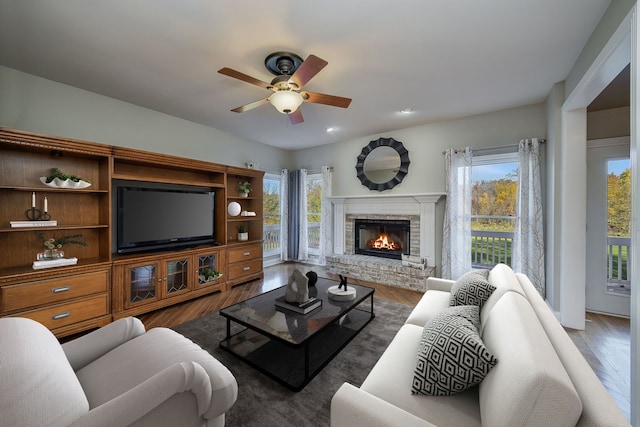 living room featuring a brick fireplace, a healthy amount of sunlight, dark hardwood / wood-style floors, and ceiling fan