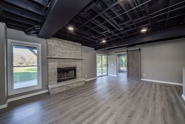 unfurnished living room featuring a fireplace, a barn door, a healthy amount of sunlight, and wood-type flooring