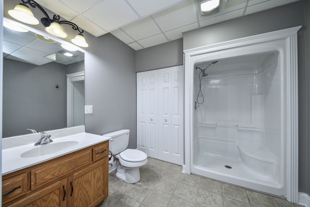 bathroom with walk in shower, a paneled ceiling, toilet, and vanity