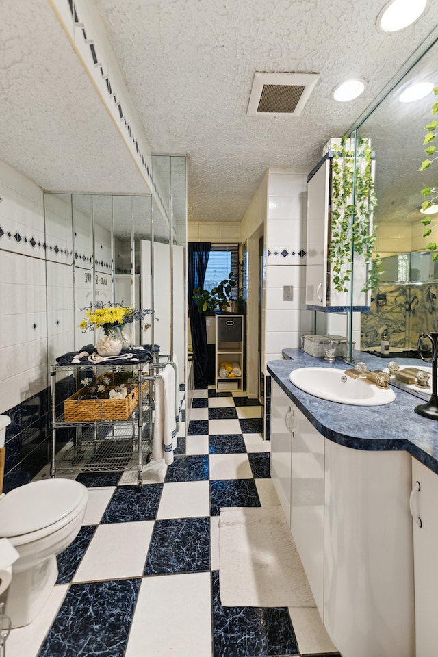 bathroom with a textured ceiling, vanity, toilet, and tile walls