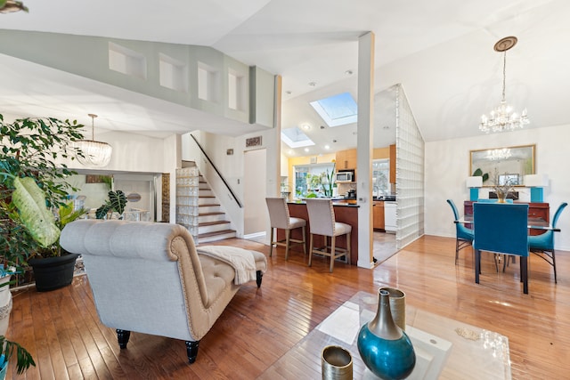 living room featuring hardwood / wood-style floors, a skylight, high vaulted ceiling, and a notable chandelier