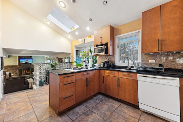 kitchen featuring white appliances, backsplash, sink, a skylight, and kitchen peninsula