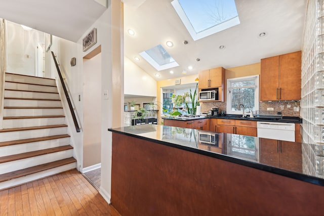 kitchen featuring a skylight, stainless steel microwave, kitchen peninsula, white dishwasher, and light hardwood / wood-style floors