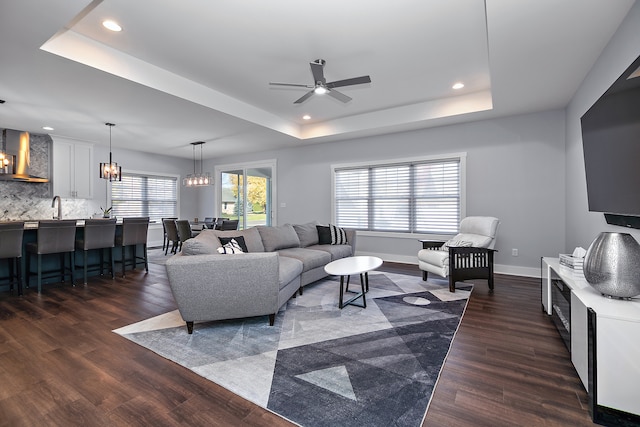 living room with dark wood-type flooring, ceiling fan, a raised ceiling, and sink