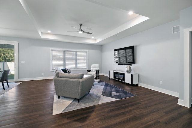 living room with dark hardwood / wood-style floors, a healthy amount of sunlight, and a raised ceiling