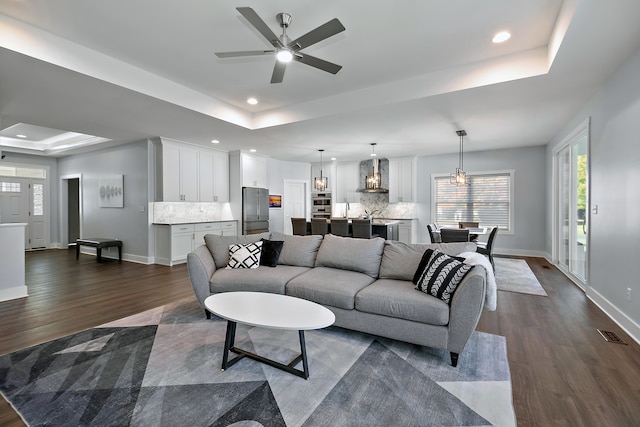 living room featuring dark wood-type flooring, a tray ceiling, and ceiling fan