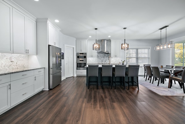 kitchen with wall chimney exhaust hood, hanging light fixtures, stainless steel appliances, and dark hardwood / wood-style flooring