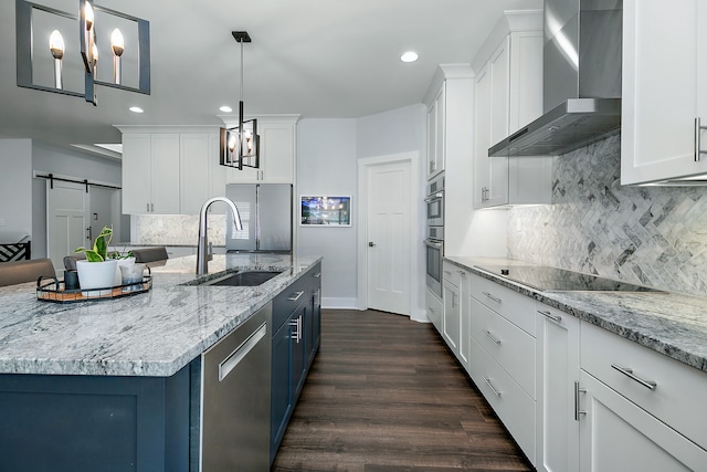 kitchen with wall chimney exhaust hood, appliances with stainless steel finishes, a barn door, and hanging light fixtures