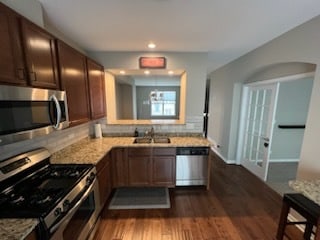 kitchen with tasteful backsplash, light stone counters, stainless steel appliances, and dark hardwood / wood-style flooring