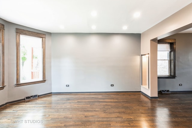 empty room with a wealth of natural light and dark hardwood / wood-style flooring