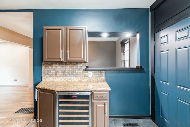 kitchen featuring wine cooler, backsplash, light stone counters, and light wood-type flooring