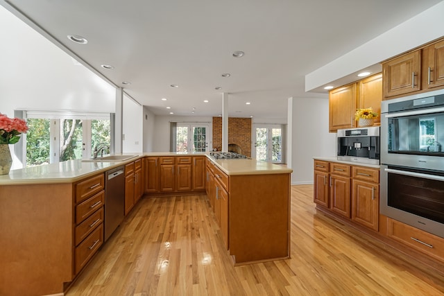 kitchen with a kitchen island, kitchen peninsula, sink, appliances with stainless steel finishes, and light hardwood / wood-style floors