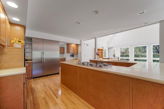 kitchen with kitchen peninsula, stainless steel appliances, sink, vaulted ceiling, and light hardwood / wood-style floors