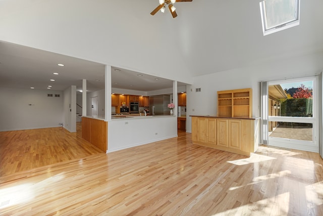 unfurnished living room featuring light hardwood / wood-style floors, high vaulted ceiling, a skylight, and ceiling fan