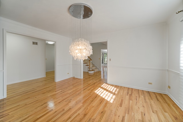 empty room featuring ornamental molding, a notable chandelier, and light hardwood / wood-style floors