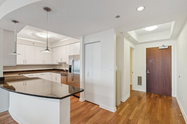 kitchen featuring kitchen peninsula, pendant lighting, a tray ceiling, white cabinets, and hardwood / wood-style flooring