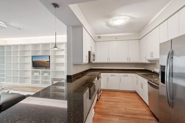 kitchen with appliances with stainless steel finishes, decorative light fixtures, white cabinetry, and light hardwood / wood-style floors