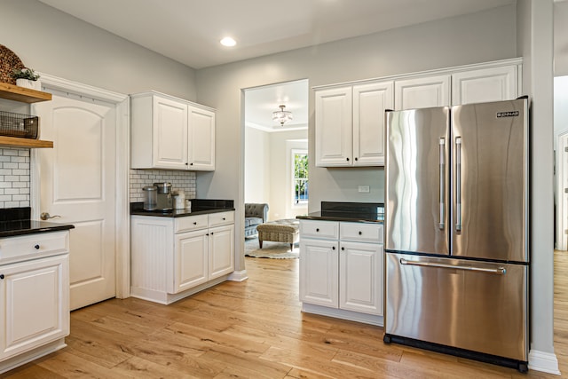 kitchen with stainless steel fridge, white cabinets, decorative backsplash, and light wood-type flooring