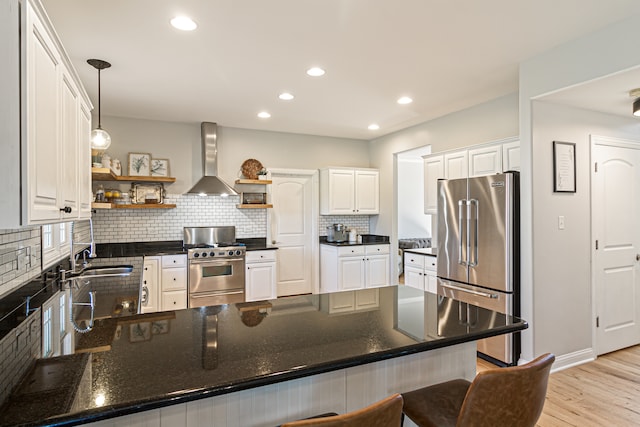 kitchen with wall chimney range hood, stainless steel appliances, decorative light fixtures, white cabinets, and light hardwood / wood-style floors