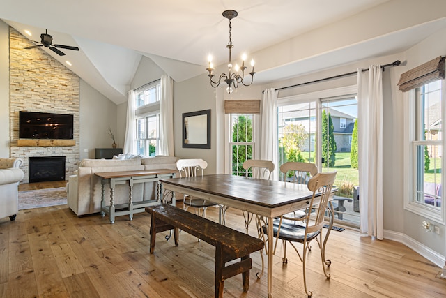 dining space with ceiling fan with notable chandelier, light hardwood / wood-style floors, vaulted ceiling, and a fireplace