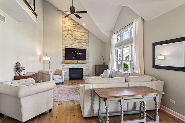 living room with a stone fireplace, high vaulted ceiling, light wood-type flooring, and ceiling fan