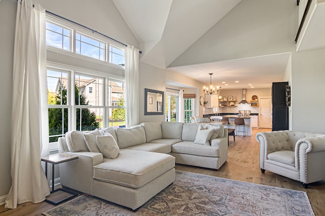 living room featuring a notable chandelier, high vaulted ceiling, a healthy amount of sunlight, and hardwood / wood-style floors