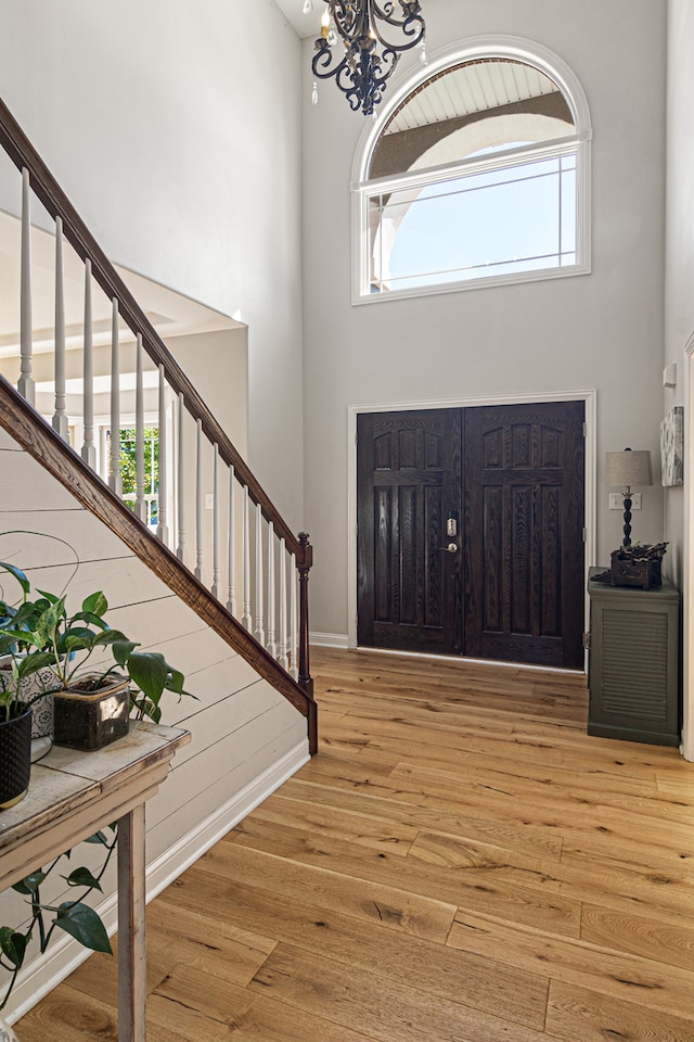 foyer featuring light wood-type flooring, a notable chandelier, a towering ceiling, and plenty of natural light