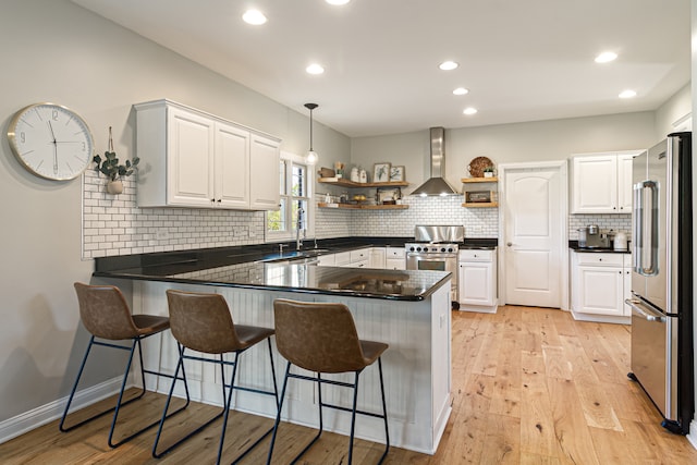 kitchen with wall chimney exhaust hood, white cabinetry, kitchen peninsula, and premium appliances