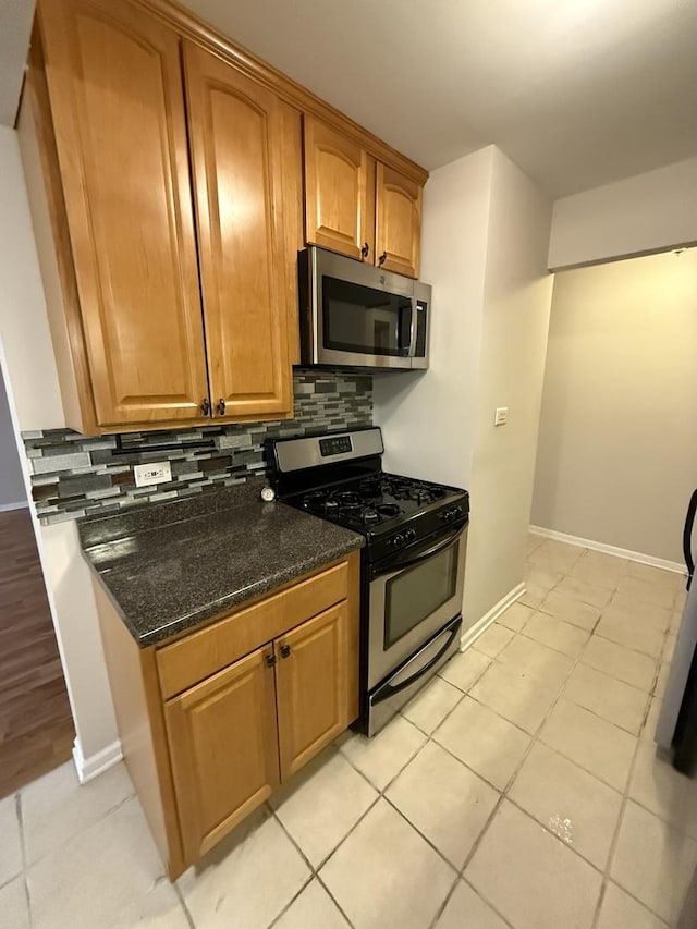 kitchen with appliances with stainless steel finishes, tasteful backsplash, dark stone counters, and light tile patterned flooring