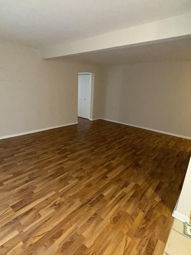 spare room with beamed ceiling and dark wood-type flooring