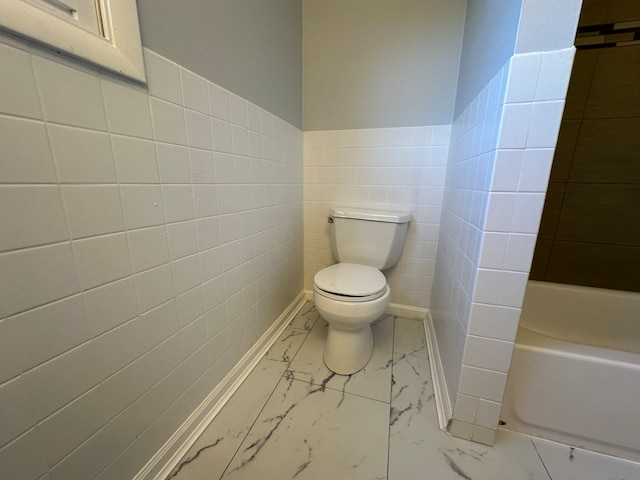 bathroom featuring toilet, a tub to relax in, and tile walls