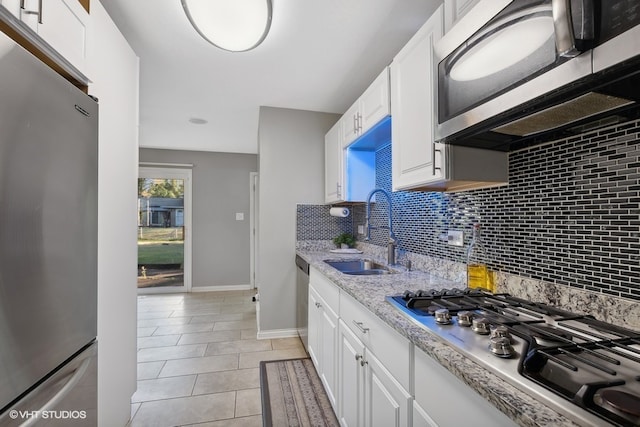 kitchen with stainless steel appliances, sink, light tile patterned flooring, white cabinetry, and tasteful backsplash