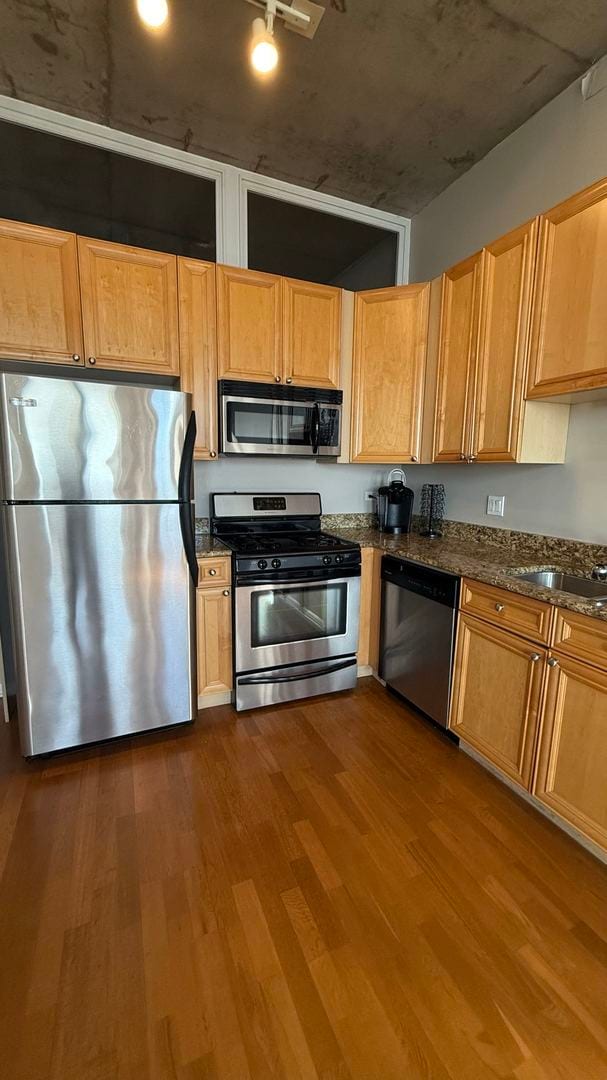 kitchen with sink, hardwood / wood-style floors, appliances with stainless steel finishes, and dark stone counters