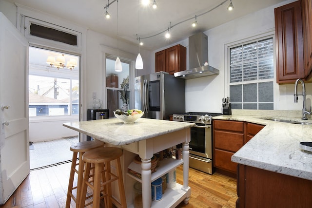 kitchen with wall chimney range hood, sink, light stone countertops, light wood-type flooring, and stainless steel appliances