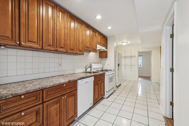 kitchen featuring sink, tasteful backsplash, dark stone countertops, white appliances, and light tile patterned flooring