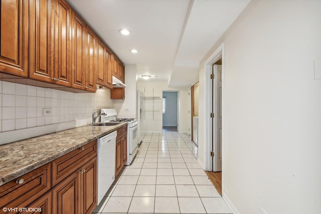 kitchen with tasteful backsplash, dark stone counters, white appliances, sink, and light tile patterned floors